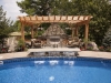 Outdoor fireplace with pergola, overlooking custom pool and water features
